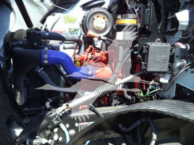 Engine bay of a 2026 Mack MD6 showing blue intake hose, red engine components, wiring, and control modules.