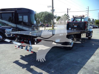 Flatbed tow truck with a rollback bed and a tow dolly in the rear, Mack MD6 in a dealership lot.
