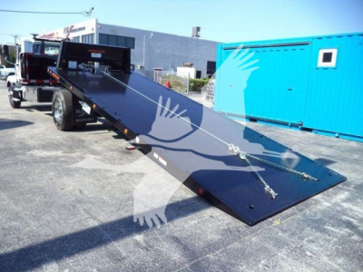 MD6 lowboy tow truck with flatbed in tilt position showing black steel deck and hydraulic winch, with blue storage container in background.