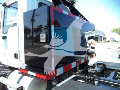 MD6 Mack rollback truck body side view showing black panel with graphic design and reflective red/white stripes under cargo area.