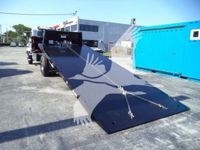 Mack MD6 rollback truck with a long black ramp extending from the rear, chains connected, in a lot.