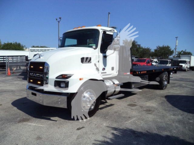 Mack MD6 truck in a dealership lot, white cab, black grille with Mack emblem, side mirrors, and a long flatbed rollback body. Visible text: 'MACK' on grille; generic dealership background.