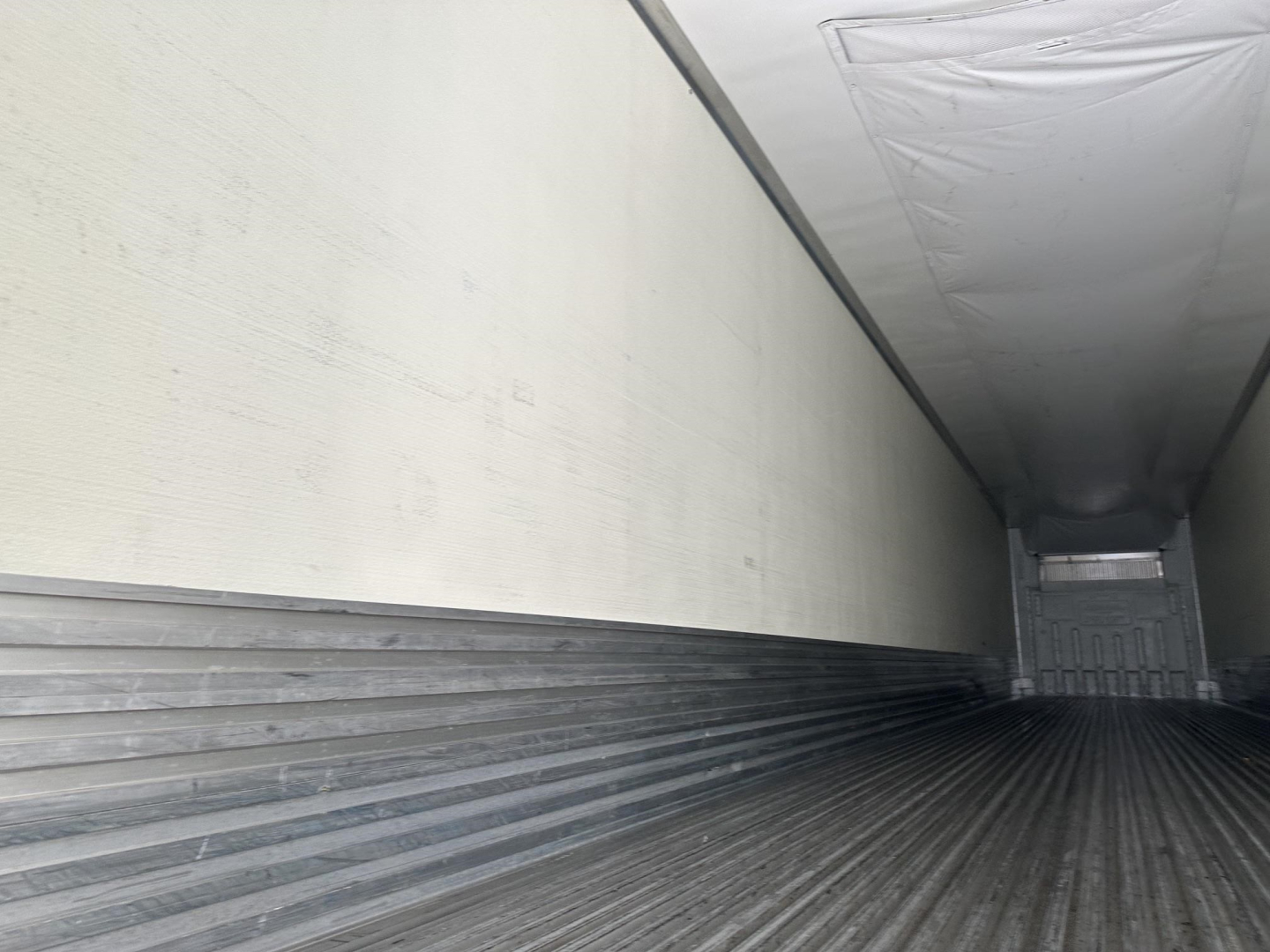 Trailer interior with ribbed metal floor and white insulated walls over the length of a refrigerated trailer.