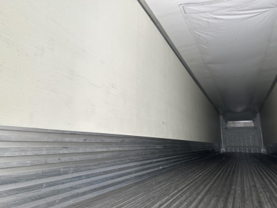 Trailer interior with ribbed metal floor and white insulated walls over the length of a refrigerated trailer.