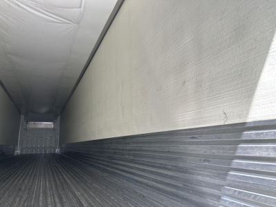 Interior of a trailer cargo area showing ribbed metal side walls and floor with a rear door gap; no legible labels or fluid reservoirs visible.
