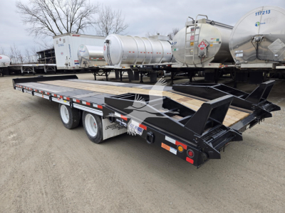 Trailer bed with dual rear axles and metal framework showing a flatbed trailer for transporting tanks near other trailers and stainless tanker units.