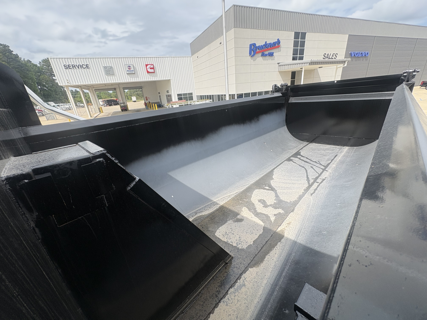 Dump truck bed interior in view with glossy black coating and clean side walls, Mack GR84F truck hub in background.