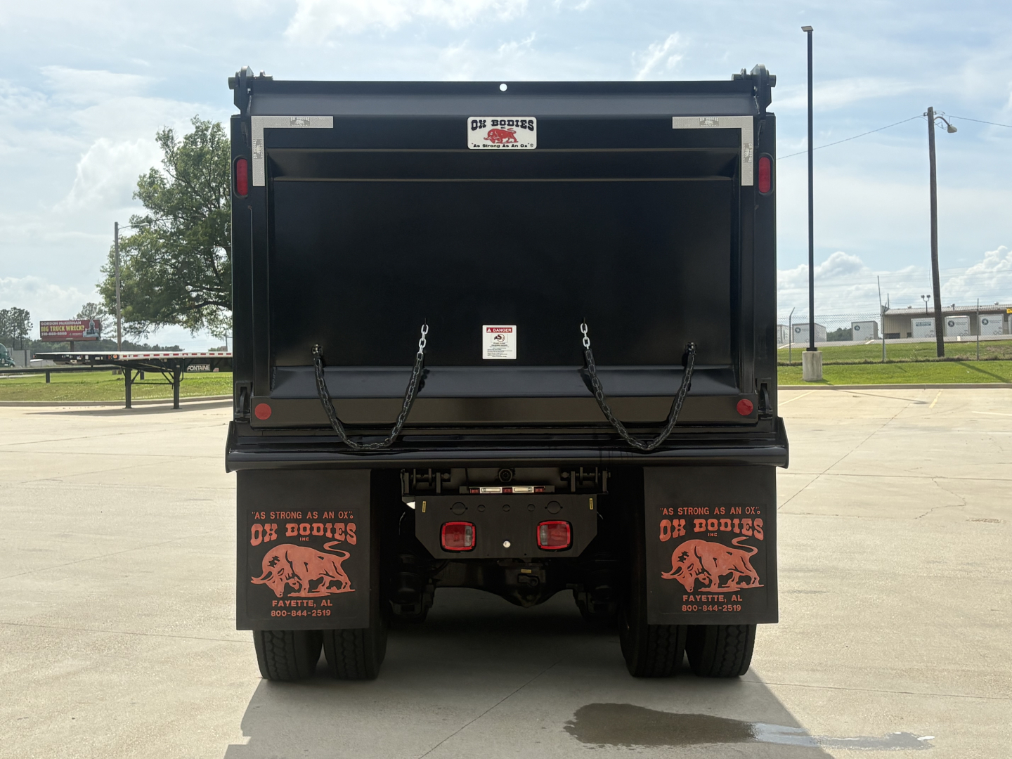 Rear view of a new 2027 Mack GR84F dump truck showing dump bed and bumper with reflector lights and mud flaps.