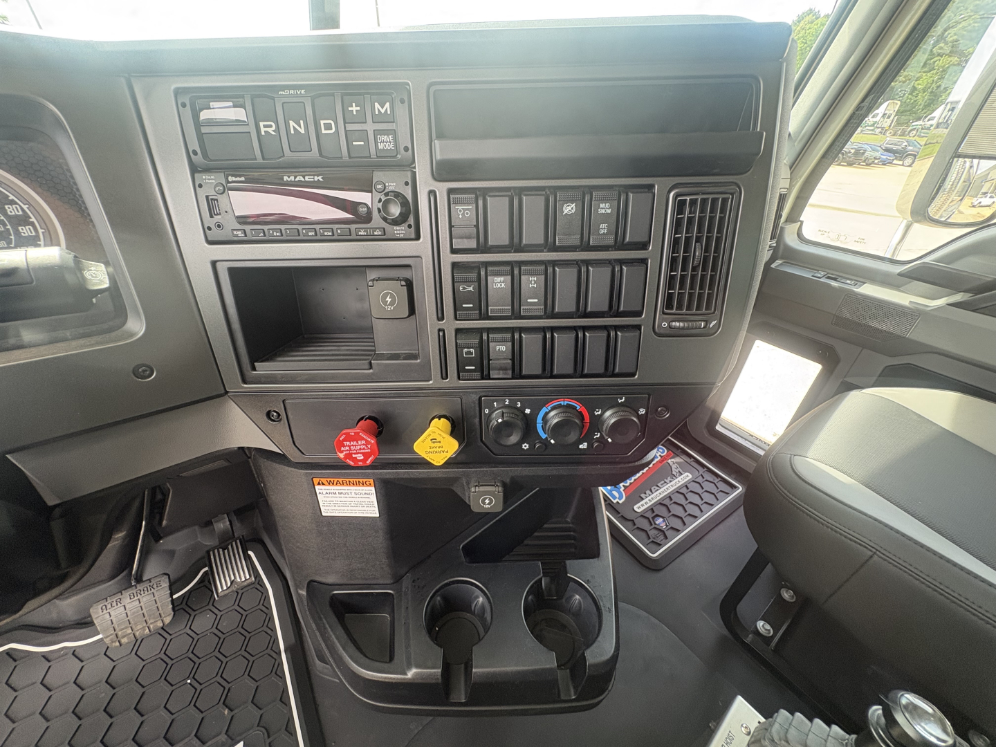 Cab interior of a 2027 Mack GR84F dump truck showing dashboard controls, switches, and two cup holders in center console.