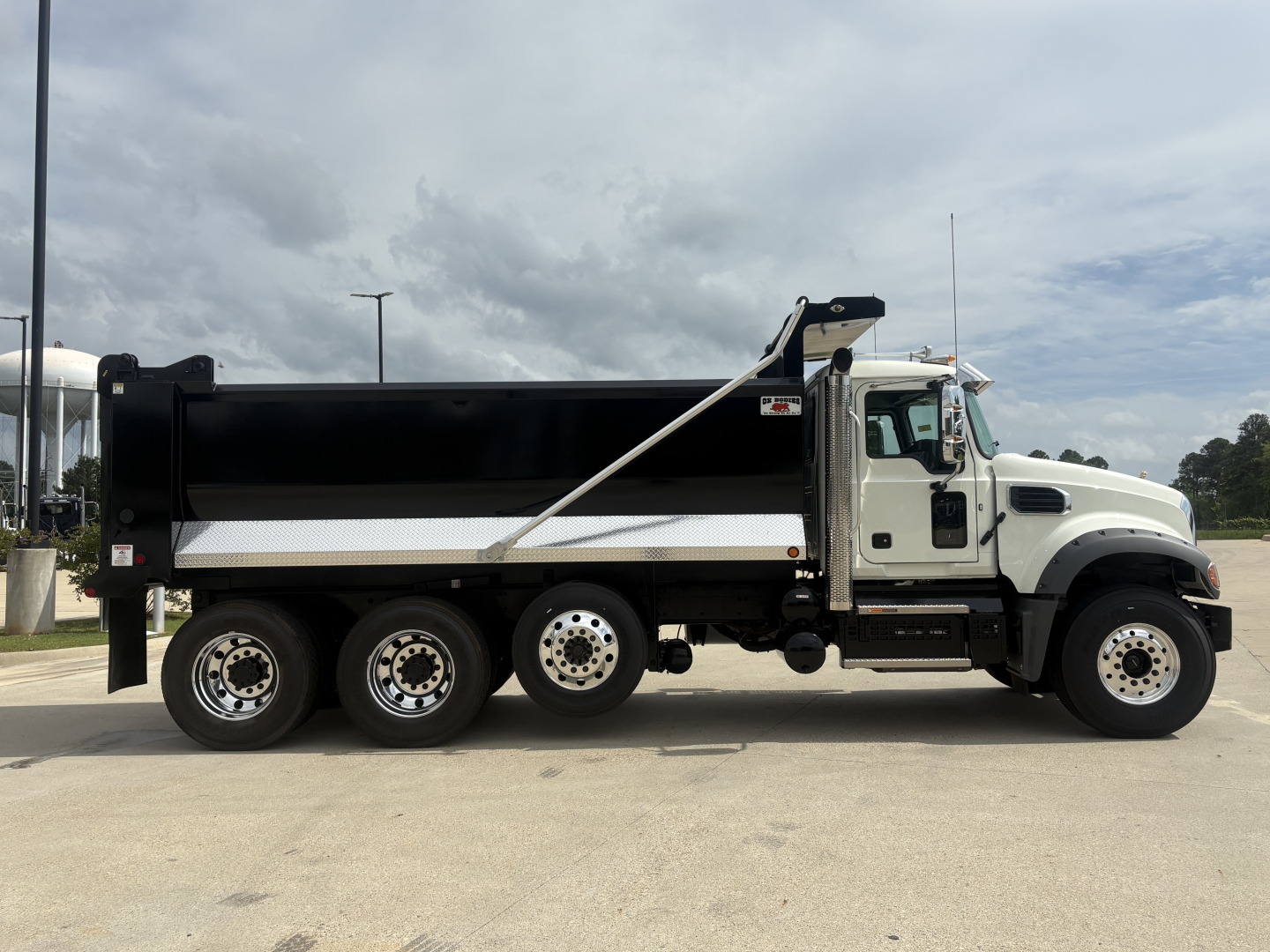Truck side profile showing a white Mack GR84F dump truck with black dump body, aluminum wheels, and hydraulic lift; VIN 1M2GR3NC1VM009410 visible on listing context.