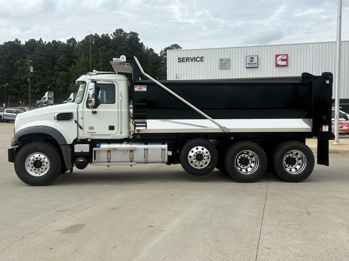 Dump truck side view showing white cab and black dump bed with chrome fuel tanks and multiple axles, Mack GR84F 6x4 chassis.