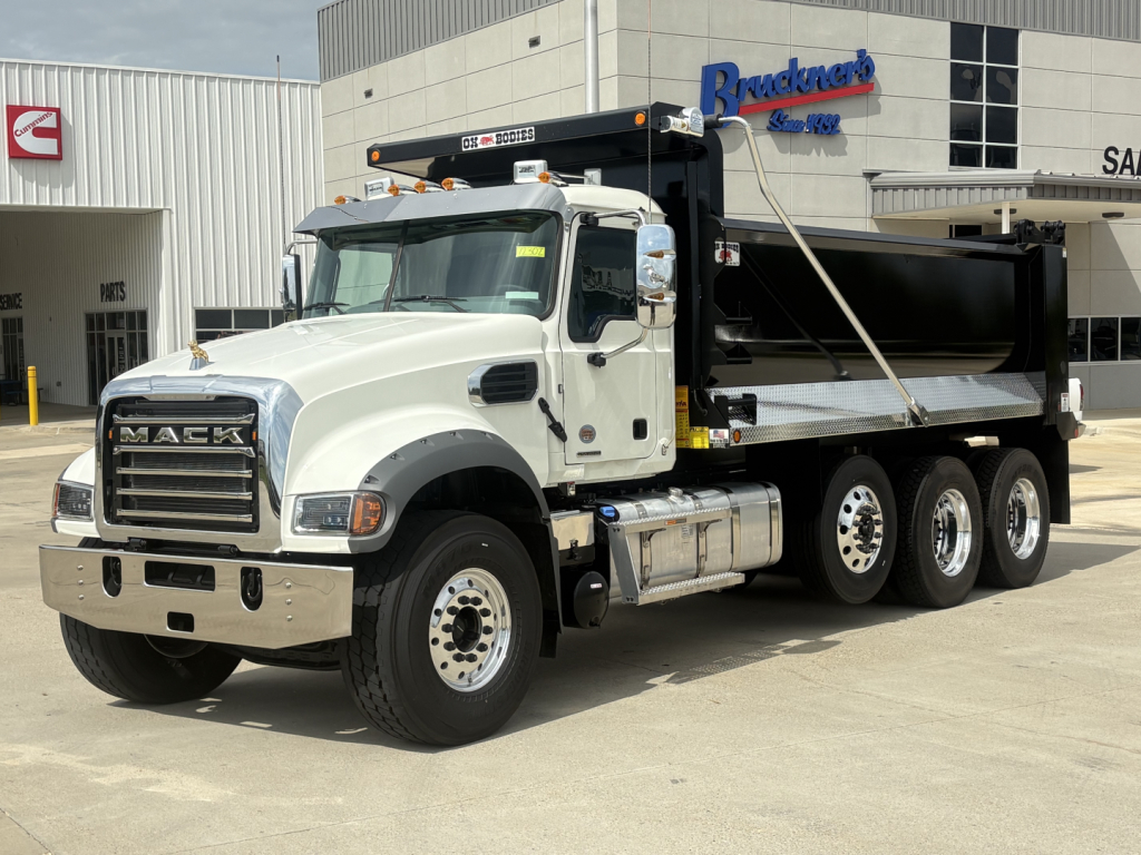 Mack GR84F dump truck in white cab with black dump body, three-axle wheels, chrome bumper, and branding visible at dealership