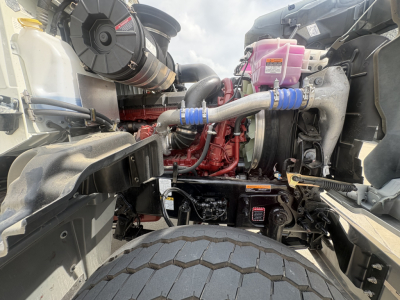 Mack GR84F engine bay showing intercooler piping, coolant reservoir, pink coolant bottle, turbocharger, engine blocks, and hoses.