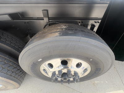 Truck wheel and dual tires showing RSTON brand wheel with lug nuts; portion of dump truck frame visible.