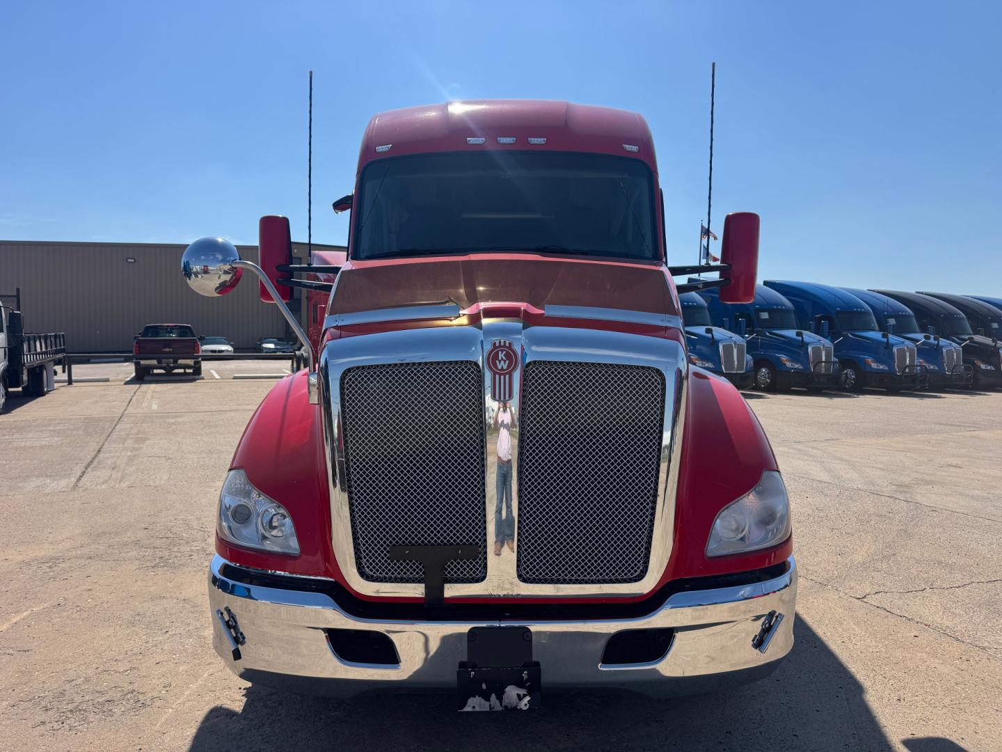 Front view of a red 2022 Kenworth T680 conventional sleeper truck with large chrome grille and bumper, windshield, and side mirrors.