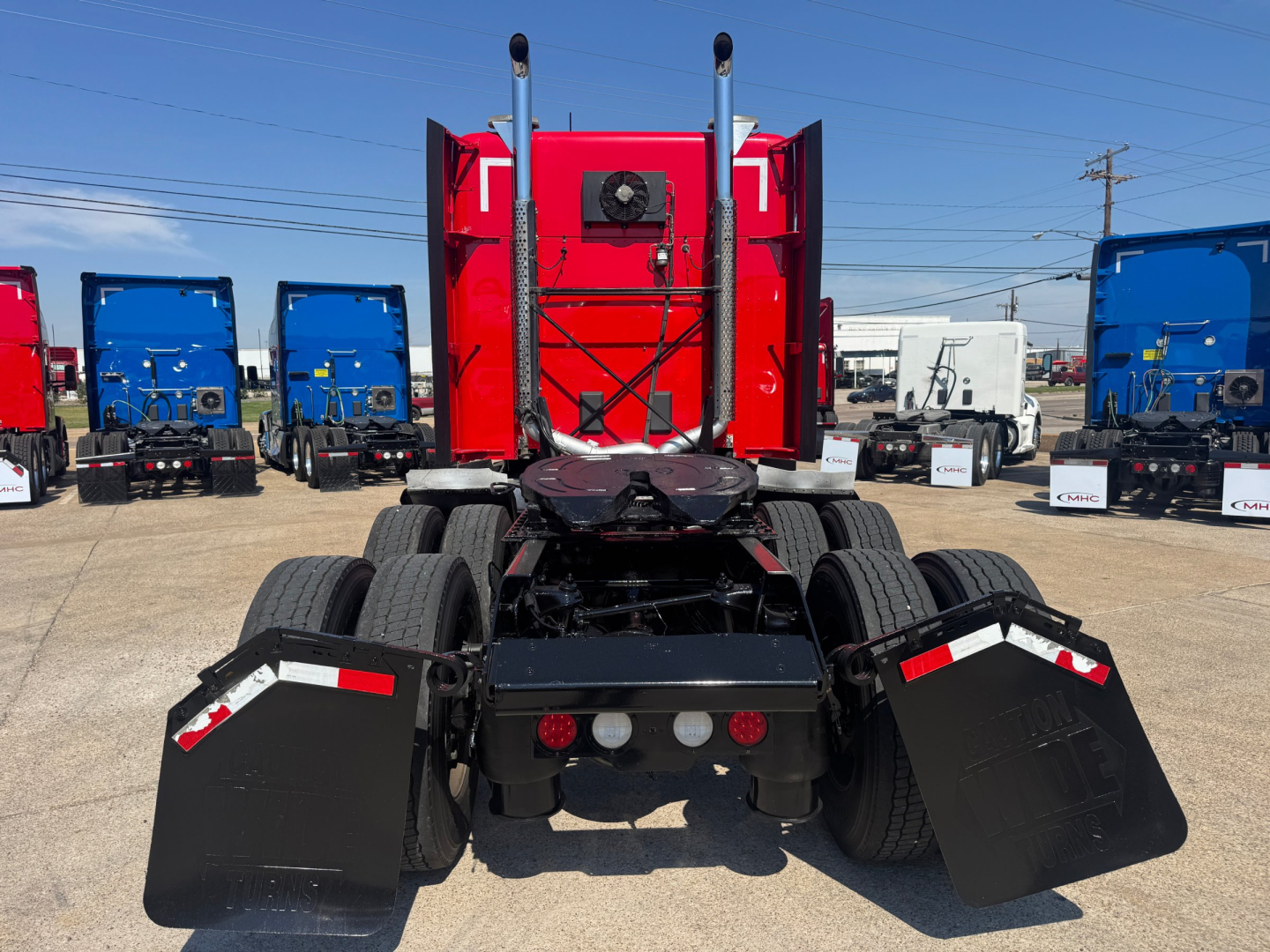 Kenworth T680 rear view showing fifth wheel and dual exhaust stacks, red sleeper cab, mud flaps, and trailer kingpin area.