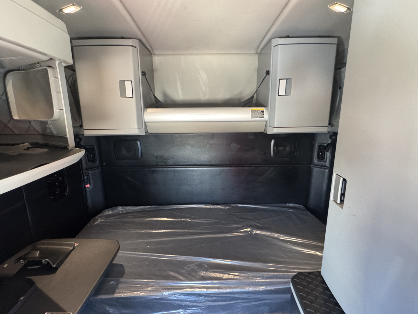 Kenworth T680 sleeper cab interior showing storage cabinets and sleeping berth with protective plastic on the bed, side wall panels, and overhead compartments.