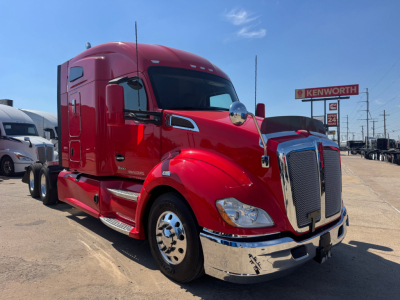 Kenworth T680 sleeper cab tractor in red with chrome bumper and grille, front view, highway backdrop.