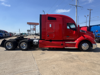 Red Kenworth T680 tractor side view showing chrome fuel tanks, rear dual wheel axles, Cab with sleeper, and emblem on door.