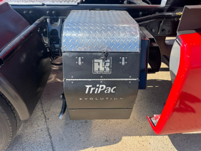 Truck tool box mounted under Kenworth T680 sleeper cab with Tripac Evolution logo visible on black lower panel and diamond plate lid.