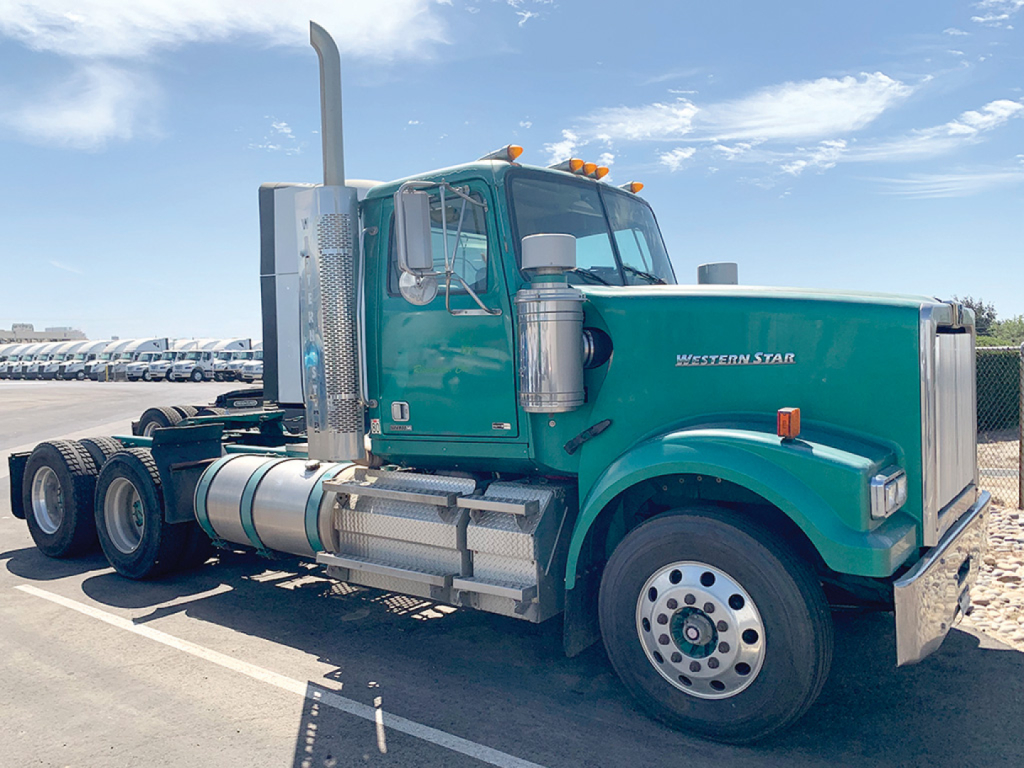 Green Western Star 4900SB conventional daycab truck side view showing fuel tanks exhaust stack and chrome grille