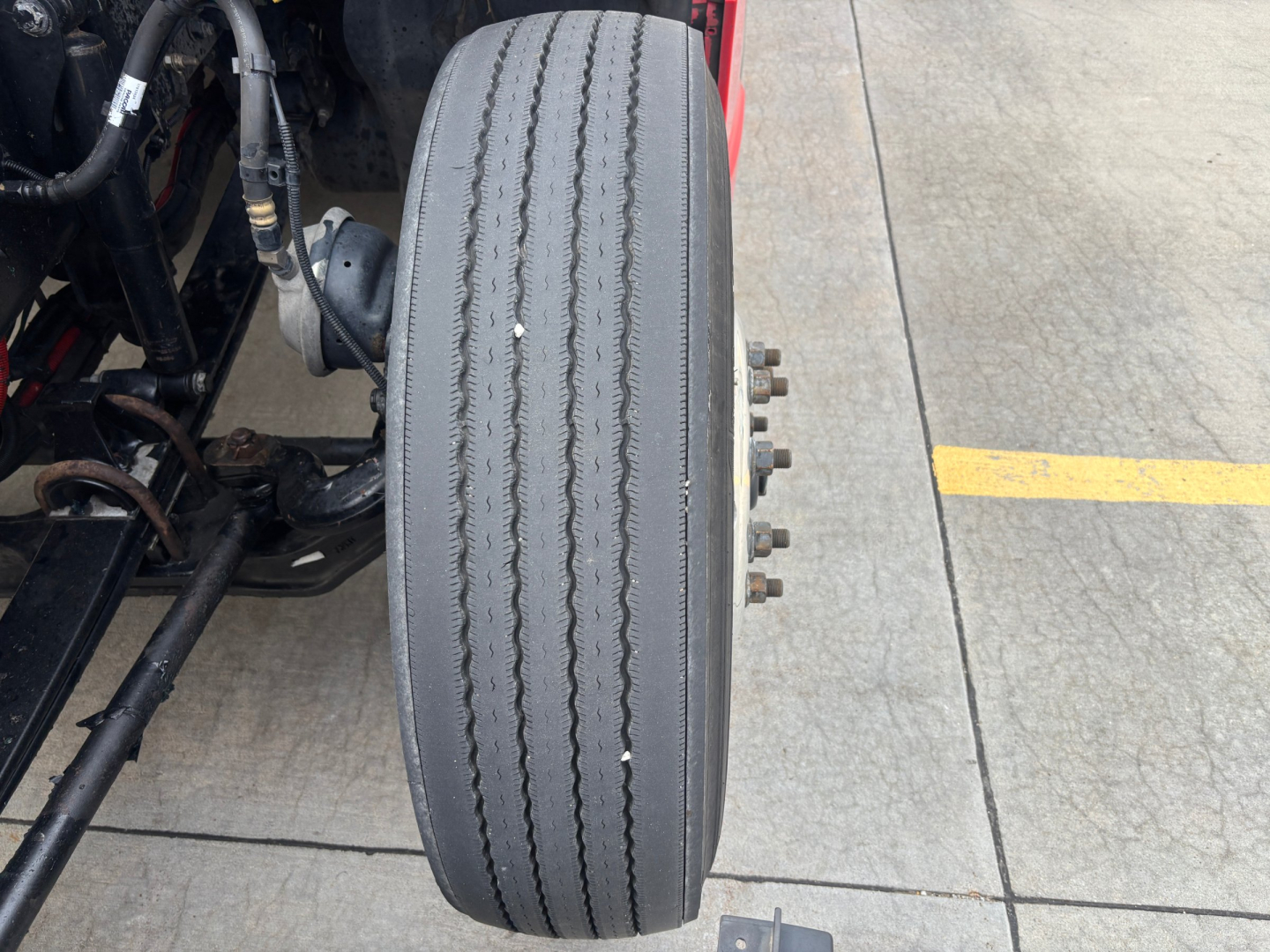 Kenworth T680 wheel/tire assembly partial chassis view showing front drive axle and dual treaded tire with metal bolts on hub.