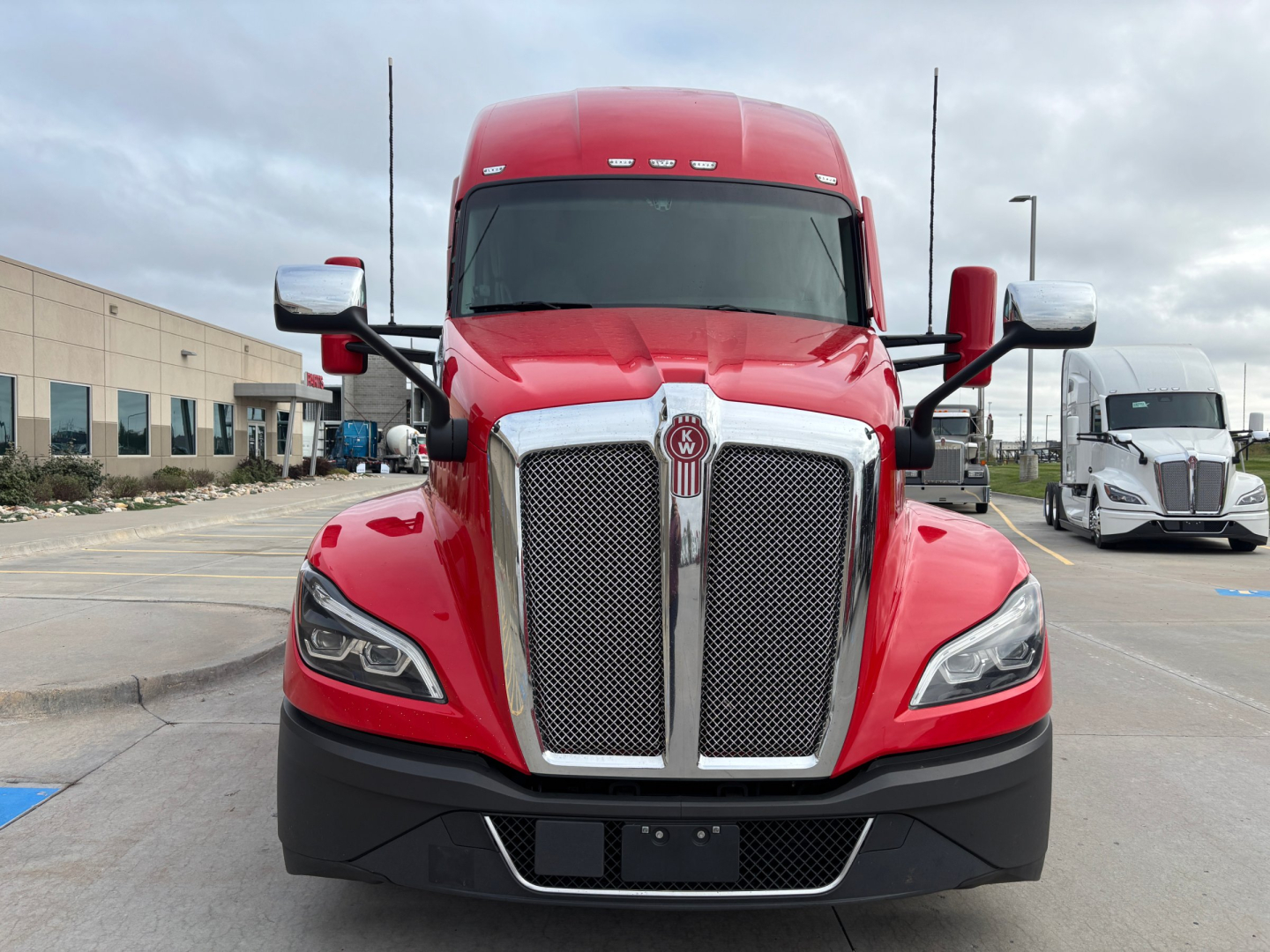 Kenworth T680 front view with red cab and chrome grille, daytime outdoor lot.