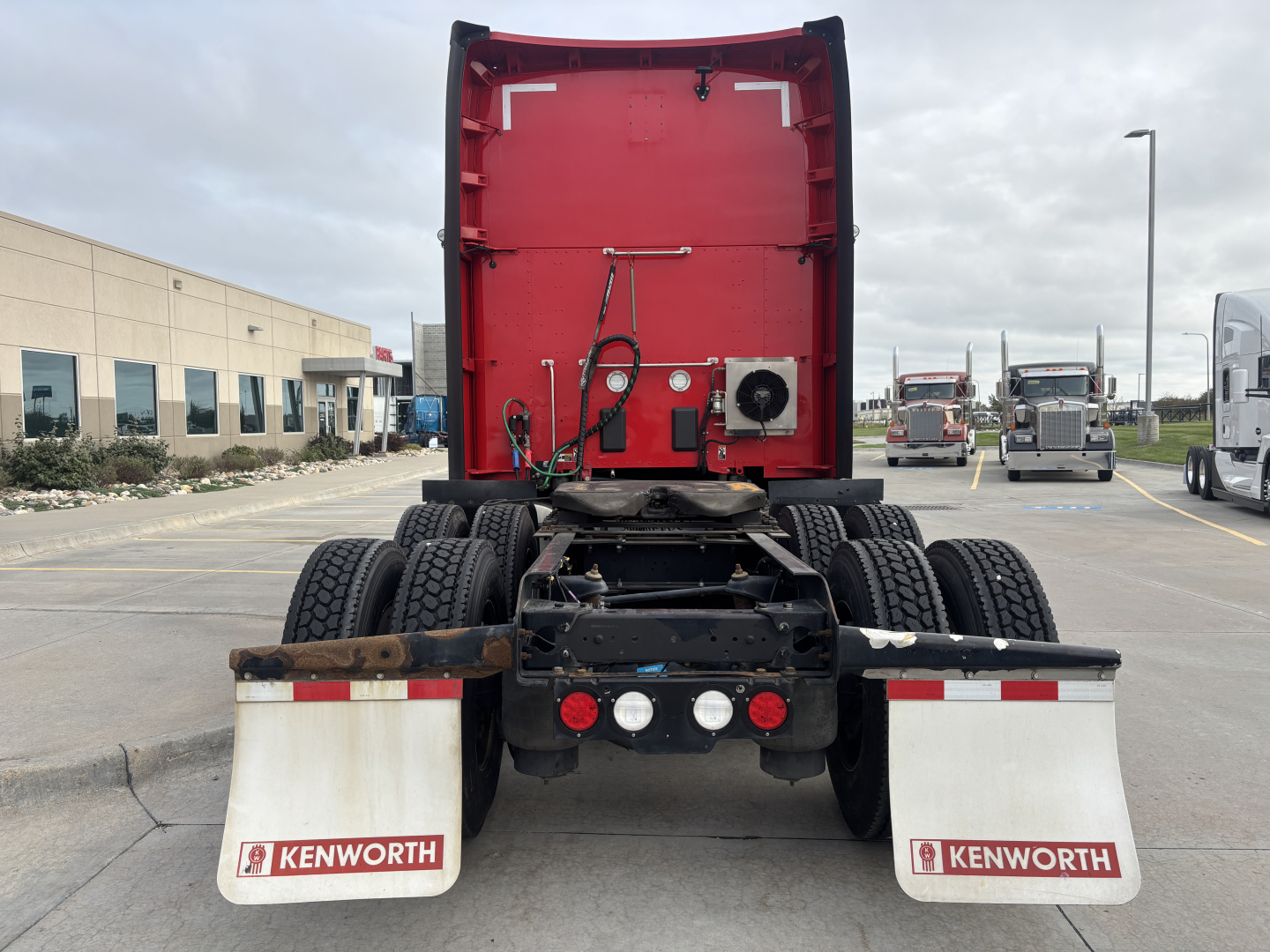 Kenworth T680 rear view showing fifth wheel hitch, dual rear axles, white Kenworth mud flaps, and red cab back with various hoses and components.