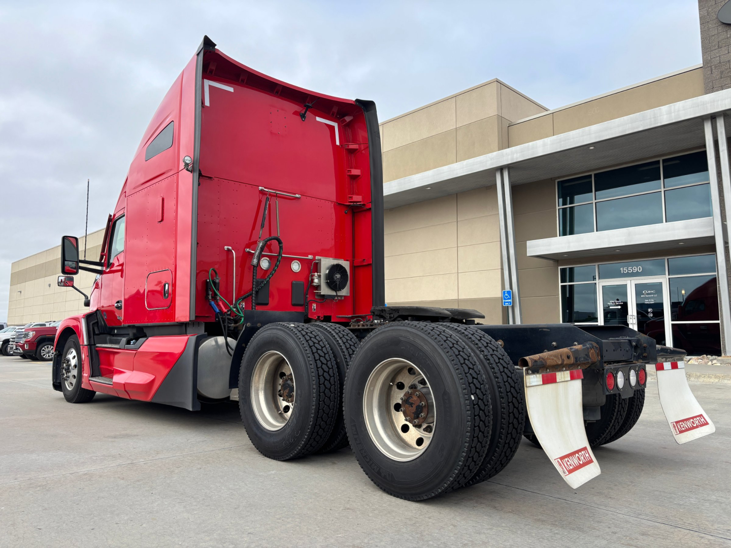 Kenworth T680 tractor rear and side view showing red cab, dual rear axles, and fifth wheel with white mud flaps.