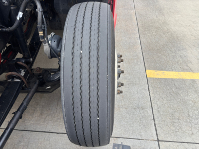 Kenworth T680 wheel/tire assembly partial chassis view showing front drive axle and dual treaded tire with metal bolts on hub.