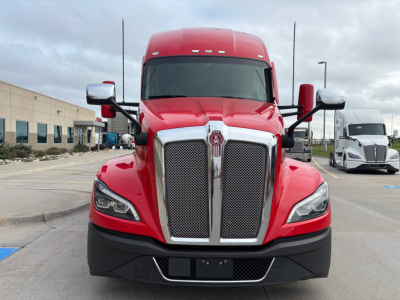Kenworth T680 front view with red cab and chrome grille, daytime outdoor lot.