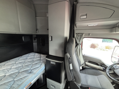 Kenworth T680 sleeper cab interior showing bunk with mattress, overhead cabinets, and driver's seat in cabin.
