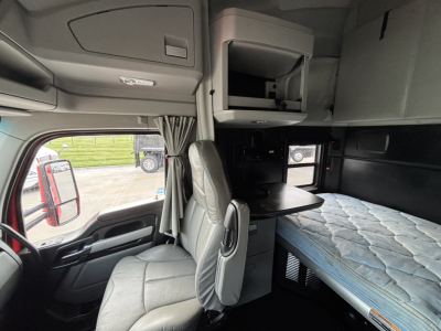 Kenworth T680 sleeper cab interior showing bunk bed, overhead storage, and driver's seat with table extension.