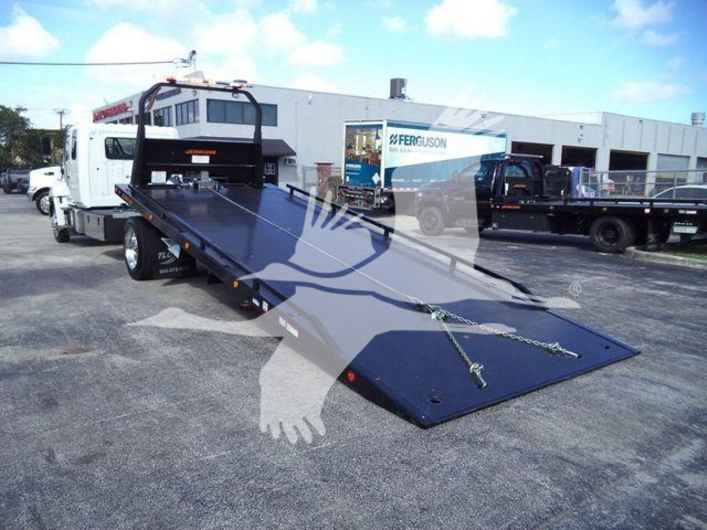 2025 Hino 268A rollback truck with a tilted ramp bed in an outdoor lot.