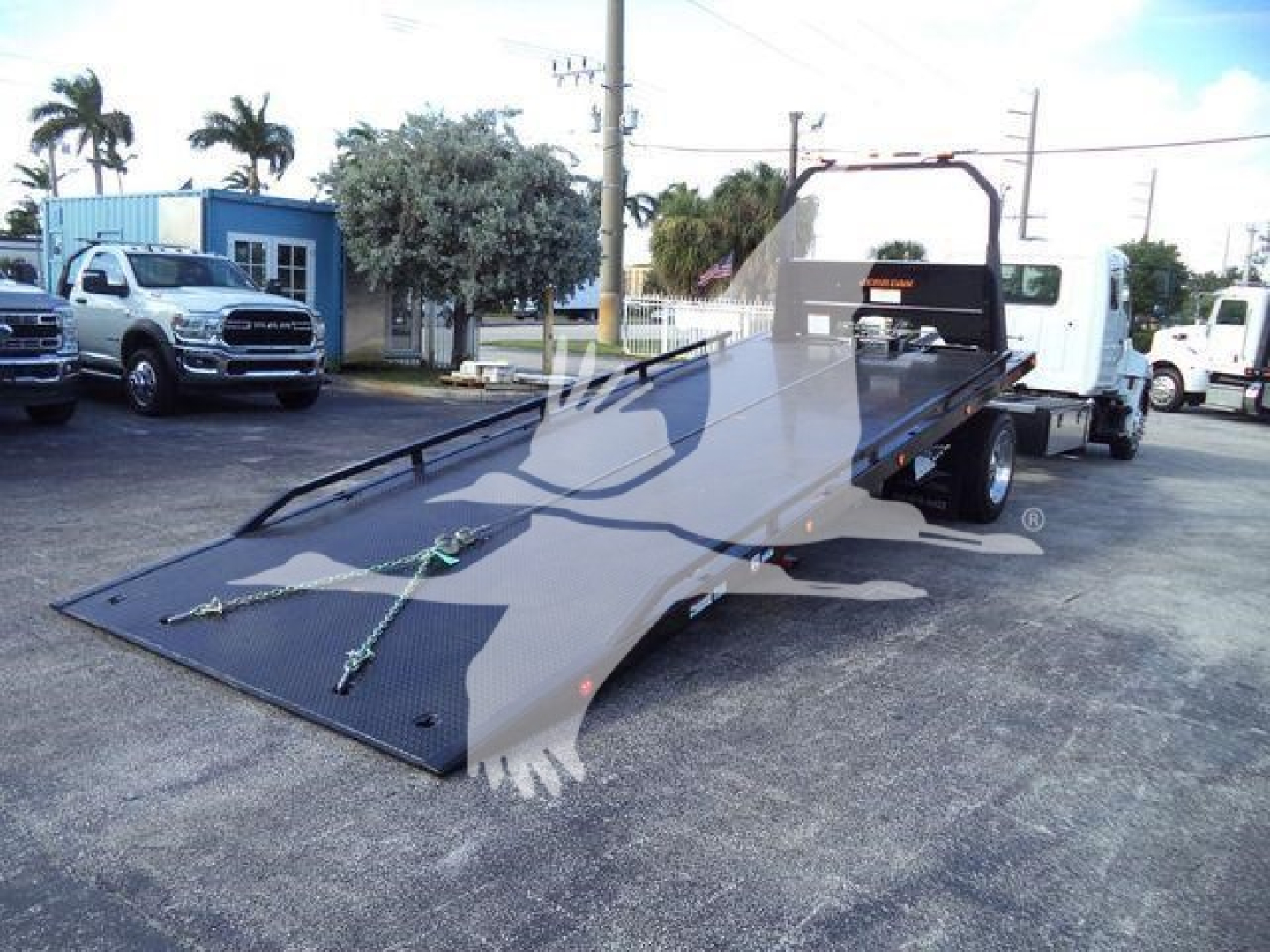 New 2025 Hino 268A rollback truck with extended flatbed and loading ramps, viewed from the side showing the lowered bed and rear wheels.