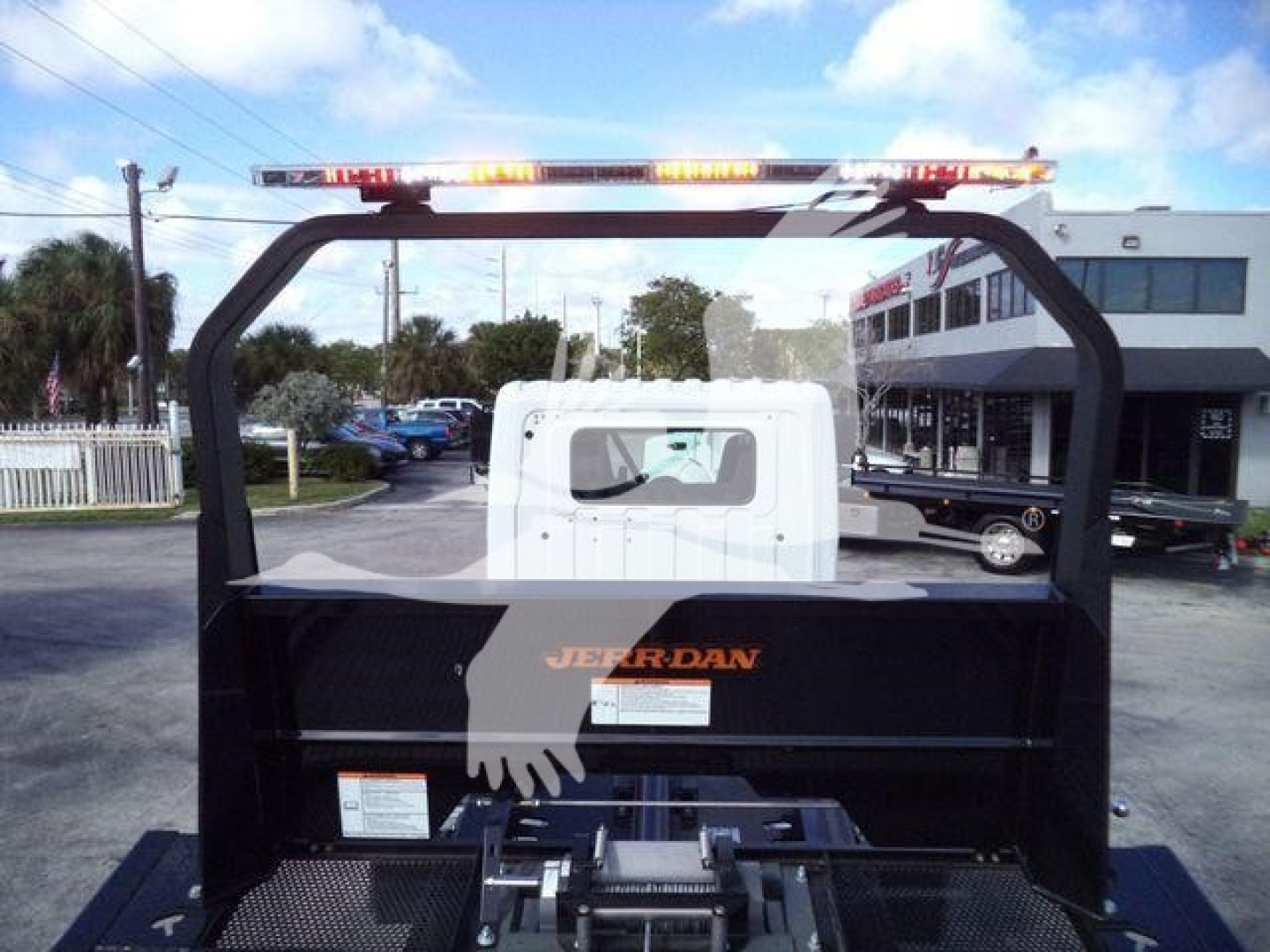 Trucks section showing the rear of a new 2025 Hino 268A rollback truck with a white cab and black Jerr-Dan body, safety lights on top, dealership lot in background.