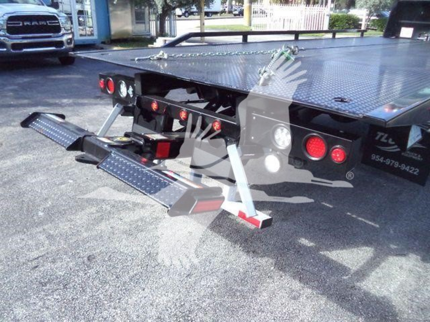 Rear view of a 2025 Hino 268A rollback truck showing hydraulic ramps extended from the bed and rear safety lights.
