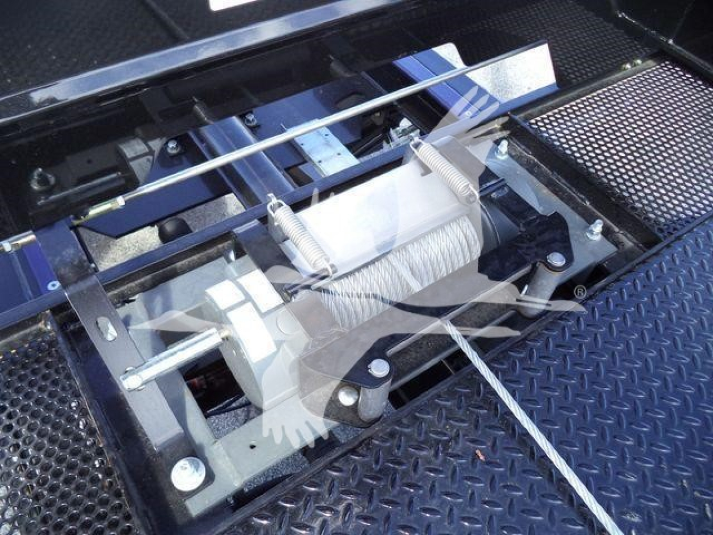 Winch/strap mechanism on a rollback truck bed with steel components, cables, and mounting brackets visible.