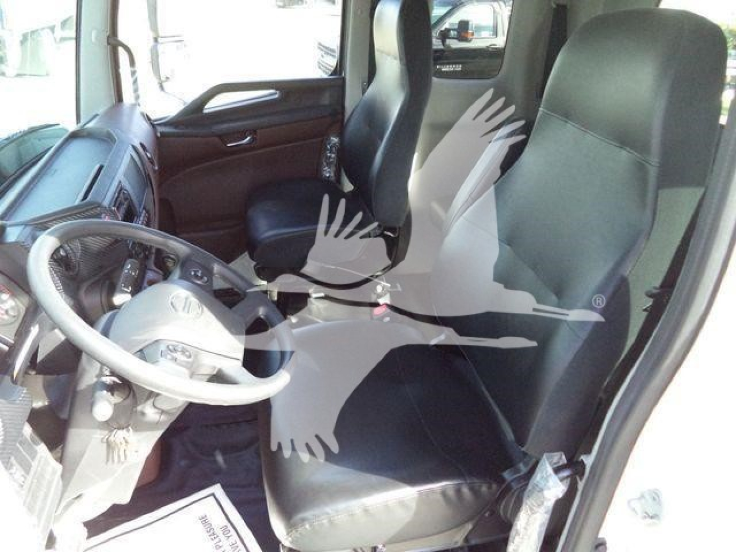Truck cab interior showing driver seat and steering wheel of a Hino truck; dashboard area visible with doors and seat belts.