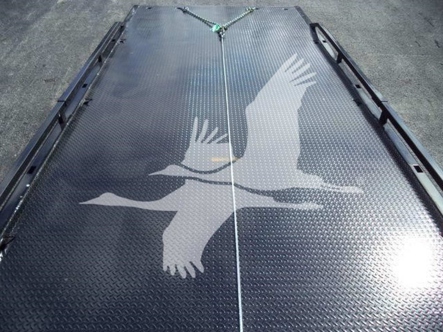 Flatbed truck bed with diamond plate surface and white crane graphic on a Hino rollback truck.