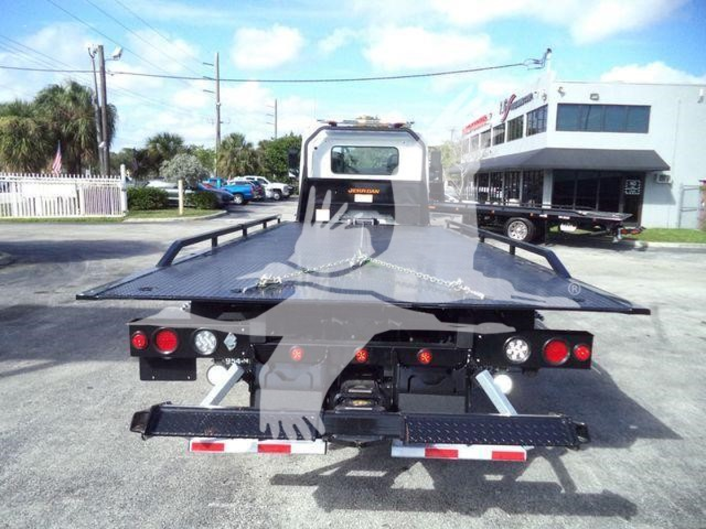 Flatbed tow truck on rear view showing hydraulic wheel-lift and multiple taillights.