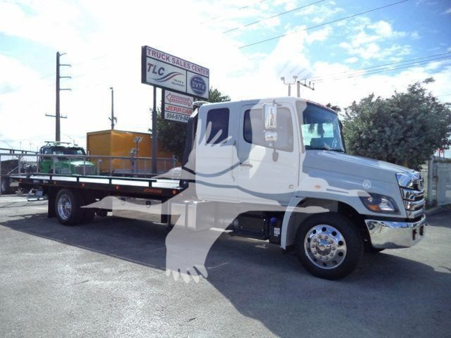 Hino 268A rollback tow truck in a dealership lot with a long flatbed and chrome wheels; stock number J50221FM visible on sign.