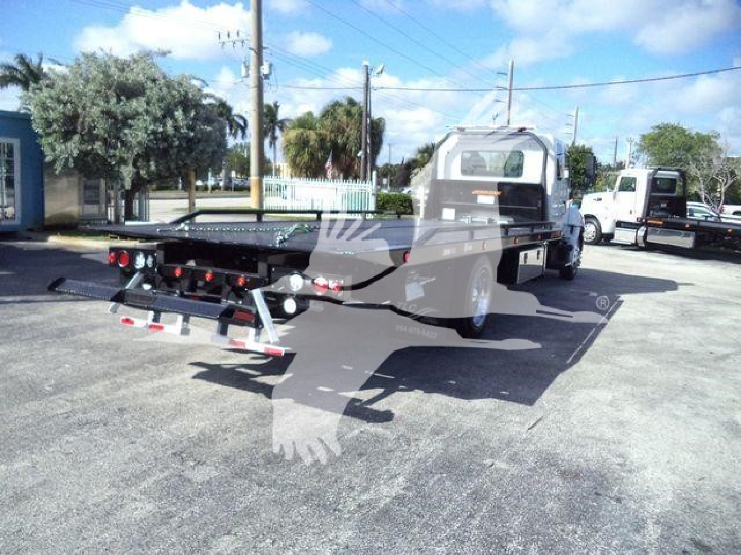 Truck bed with rollback carrier on a new Hino 268A chassis, rear view showing hydraulic ramps and lettering on the back deck.