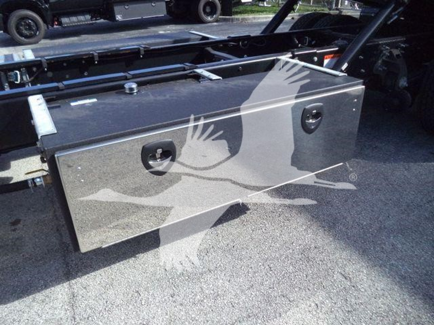 Truck bed toolbox mounted in a chassis frame of a 2025 Hino 268A rollback truck showing a metal rectangular toolbox with two latches and a threaded filler neck.