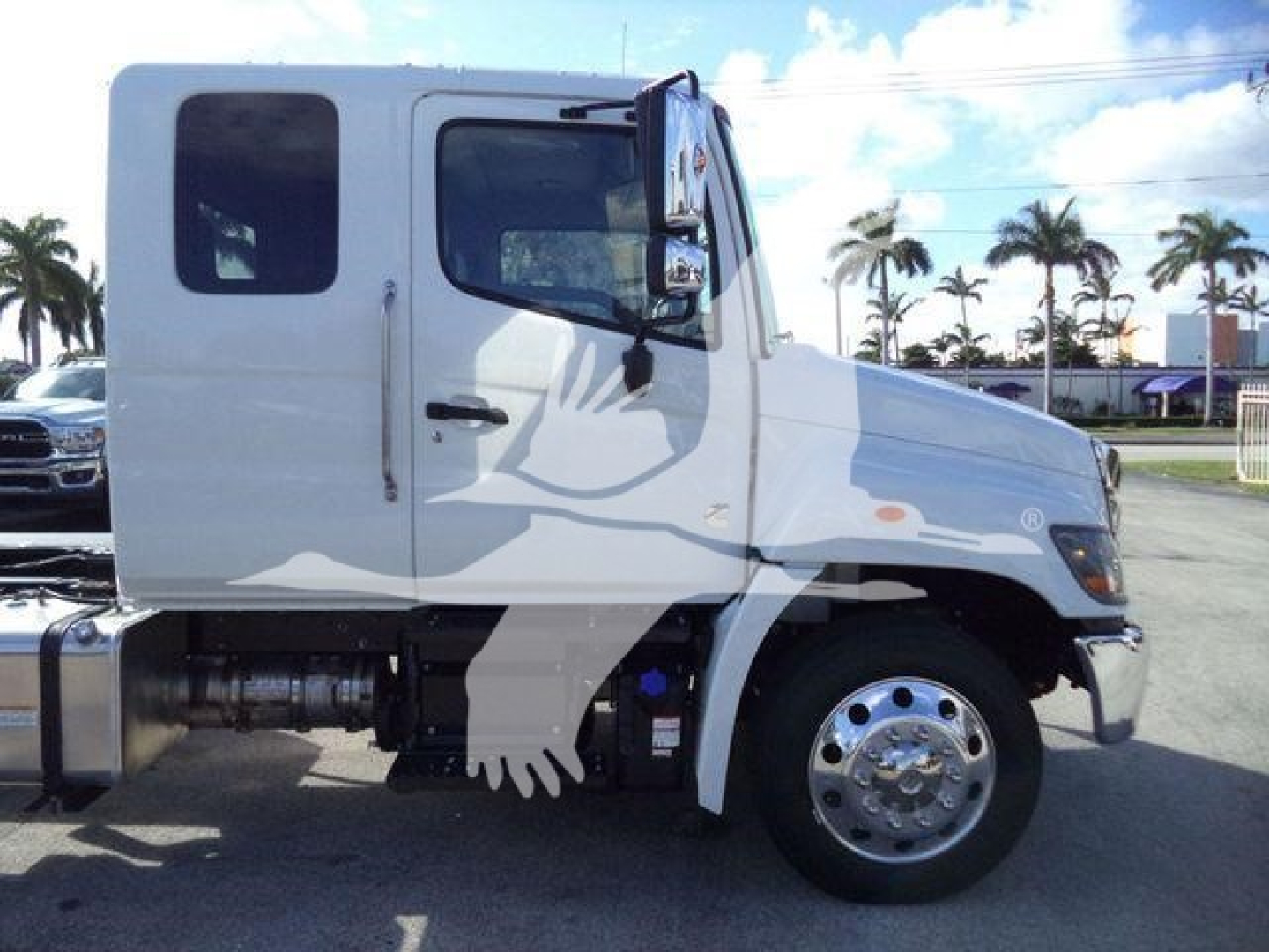 Truck cab side view showing white 2025 Hino 268A rollback tractor with dual rear wheels and chrome hubcap, stock J50221FM.