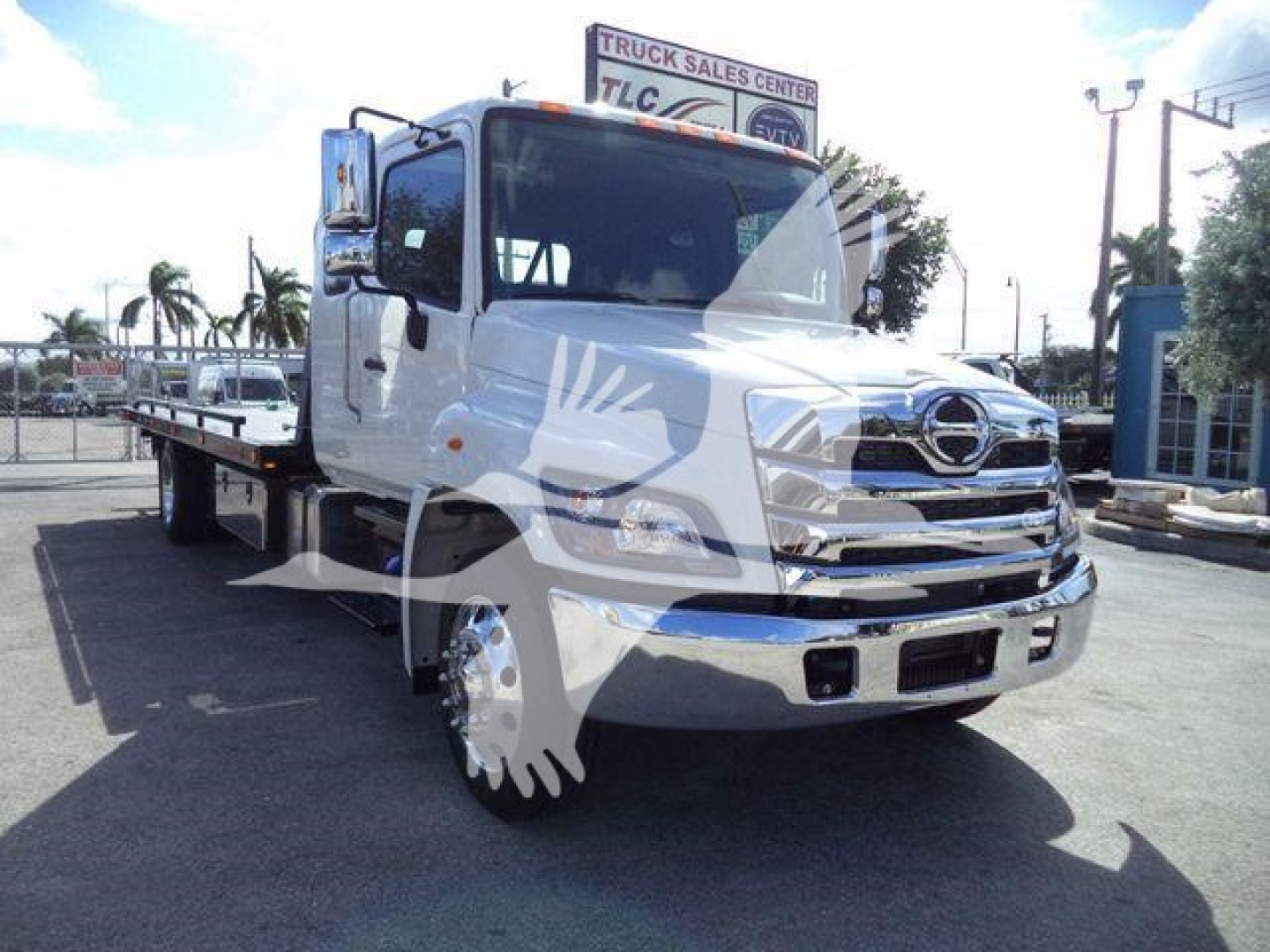 Truck cab of a white 2025 Hino 268A with flatbed rollback body, front grille and chrome bumper visible.