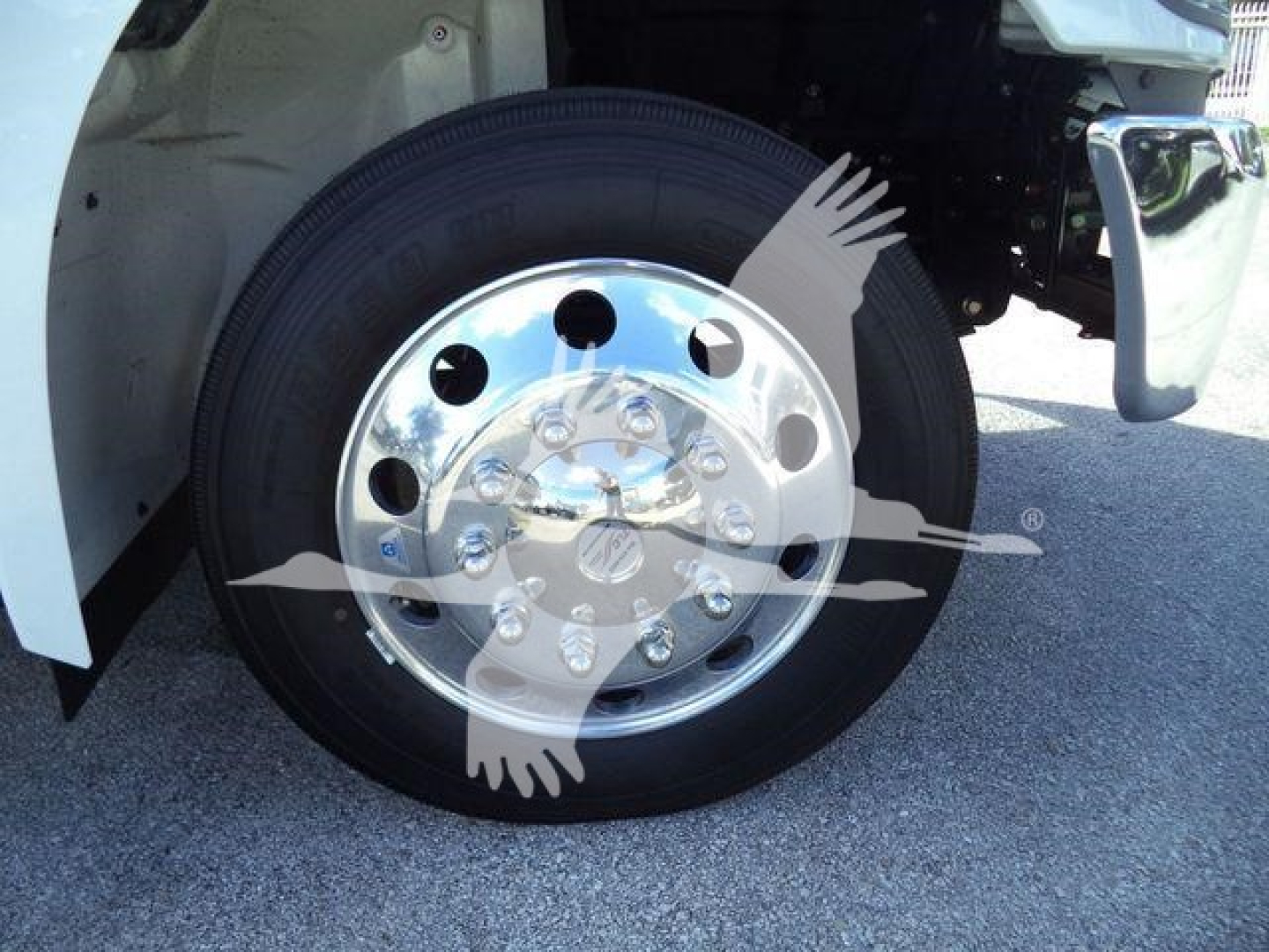 Truck wheel and fender area showing a polished chrome hubcap on a black tire with white truck body nearby.