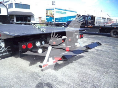 Truck rollback tow truck bed with hydraulic ramps and lights visible; rear view shows platform and controls under the load bed.
