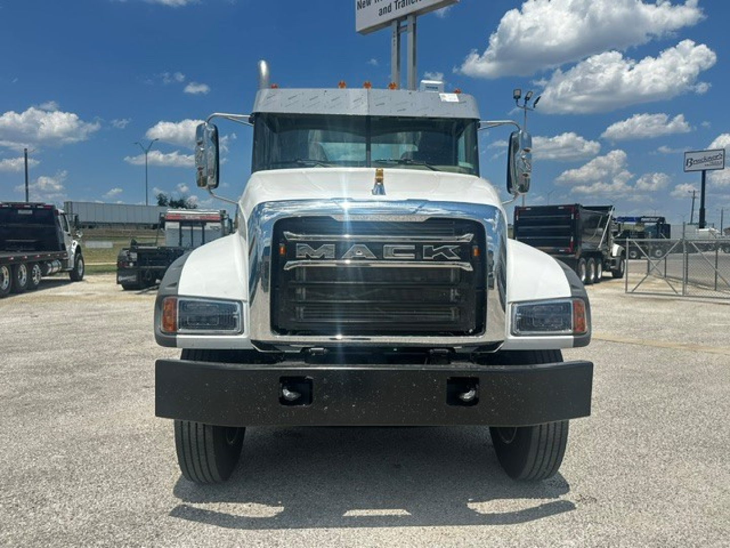 Mack GR64F cab and chassis front view showing Mack grille letters and bumper; white truck with large side mirrors and clear sky.