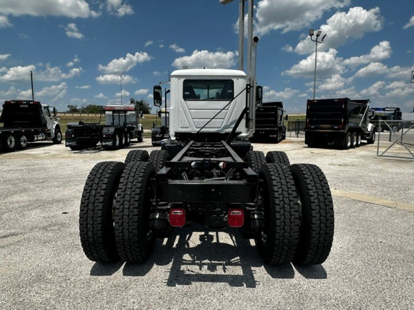 Mack GR64F urban cab chassis rear view showing dual rear axles and dual sets of tires with white cab in background.